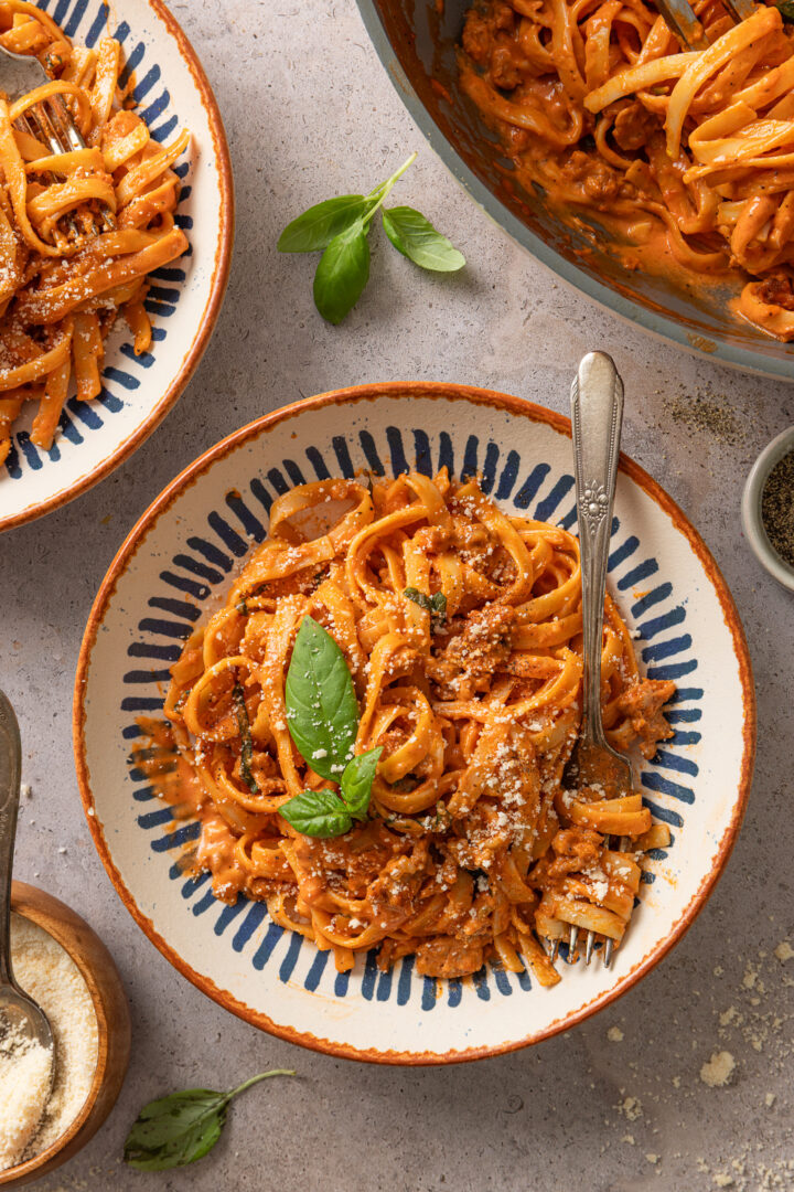 Creamy one pot pasta with spicy sausage served in a bowl with Parmesan cheese and fresh basil