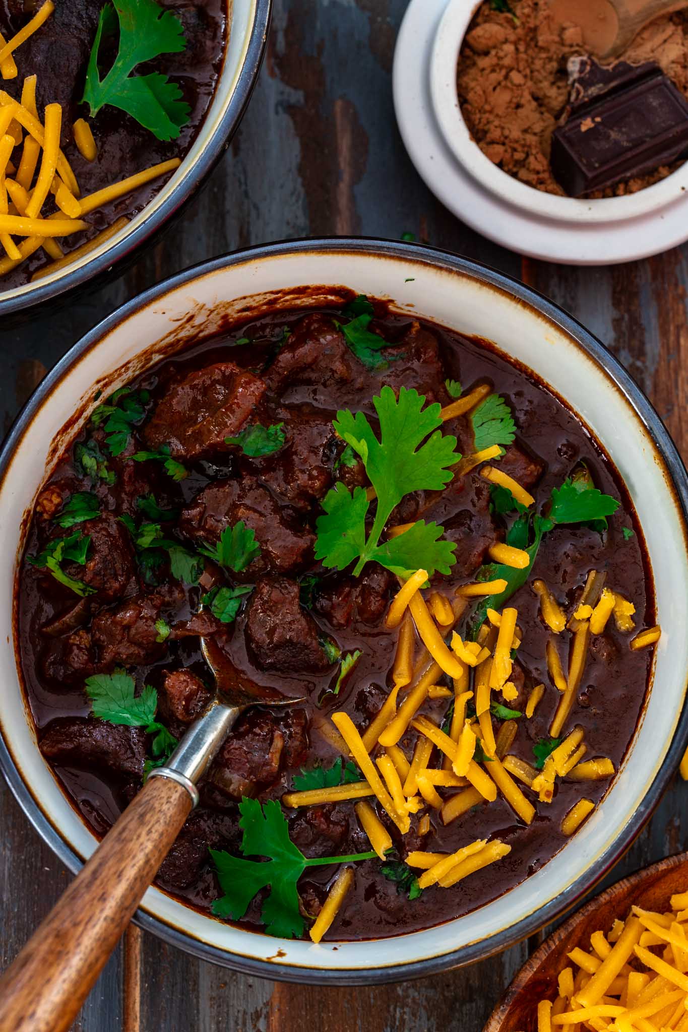 A bowl of beef chili topped with cilantro and cheddar cheese