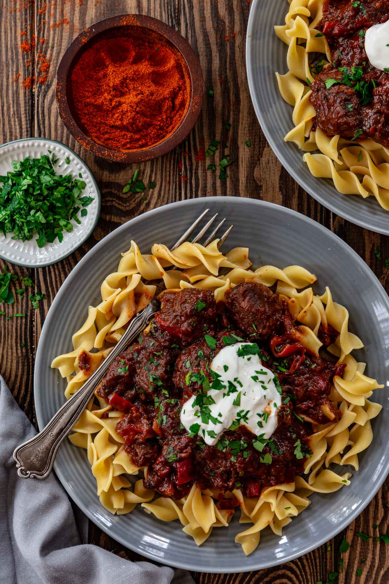 One serving of Porkolt stew over egg noodles, garnished with parsley and sour cream