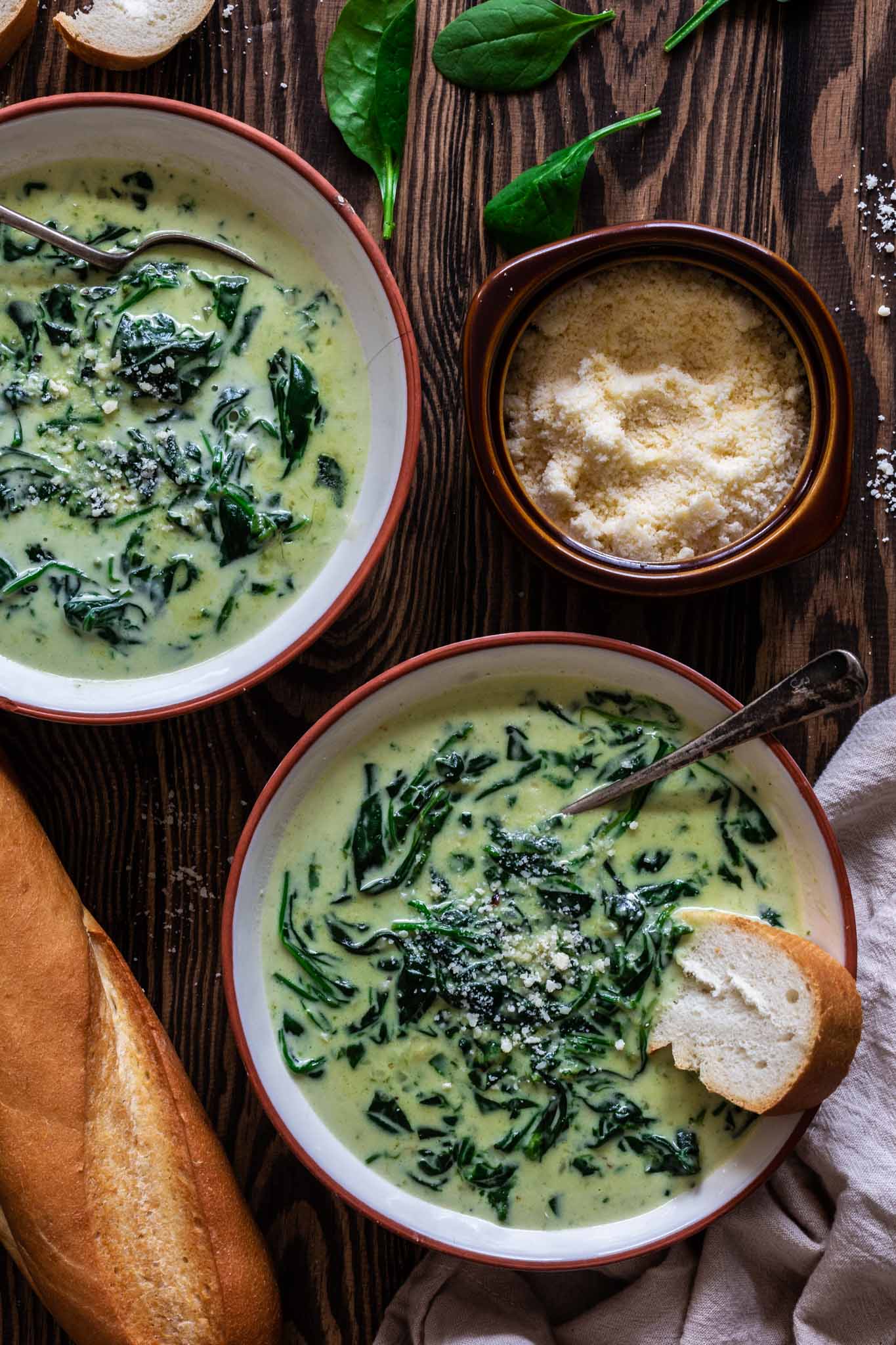 two bowls of cream of spinach soup with bread and parmesan