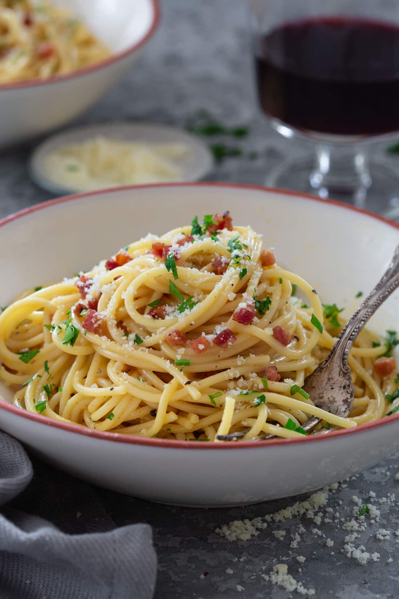 A bowl of Spaghetti Carbonara garnished with parsley and grated Parmesan cheese.