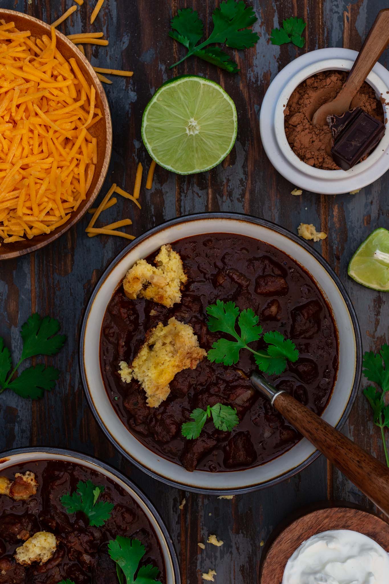 Two bowls of Double Chocolate Chili being served with cheddar cheese, sour cream and lime.