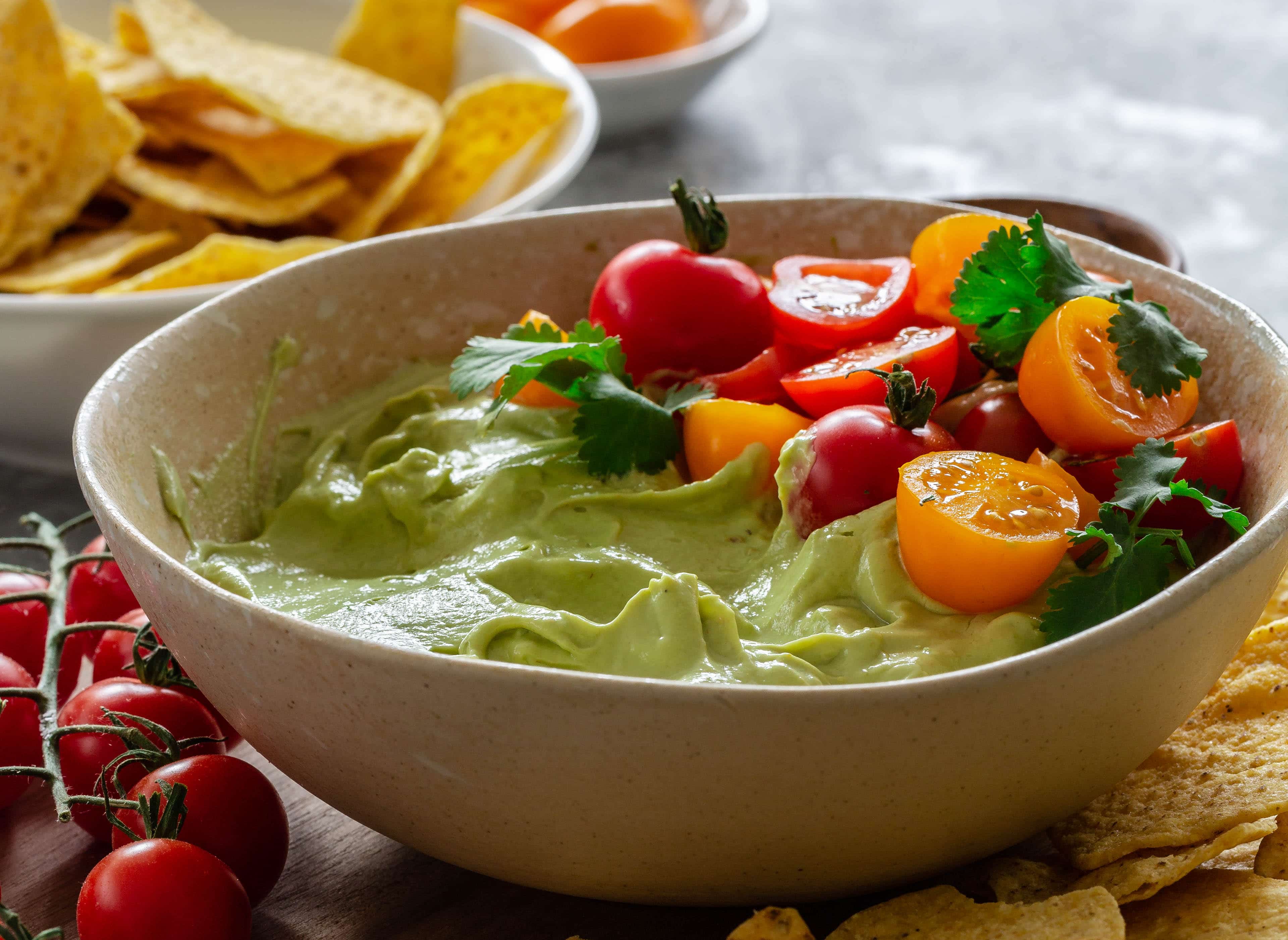 A horizontal image of whipped avocado dip topped with fresh tomatoes and served with tortilla chips.
