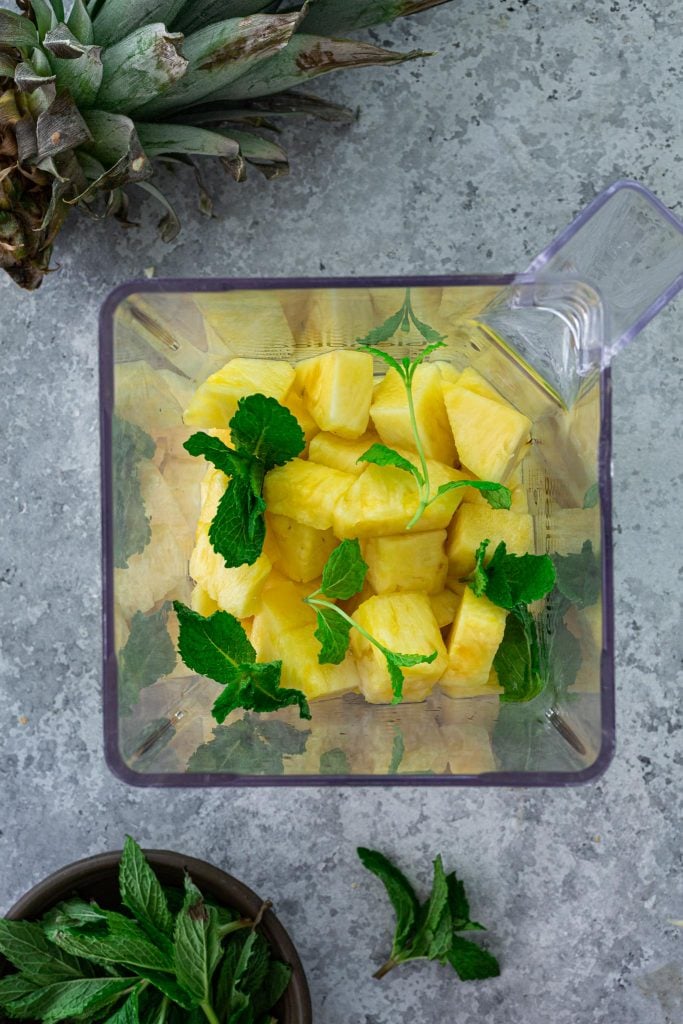 Chunks of pineapple and mint leaves in a blender.