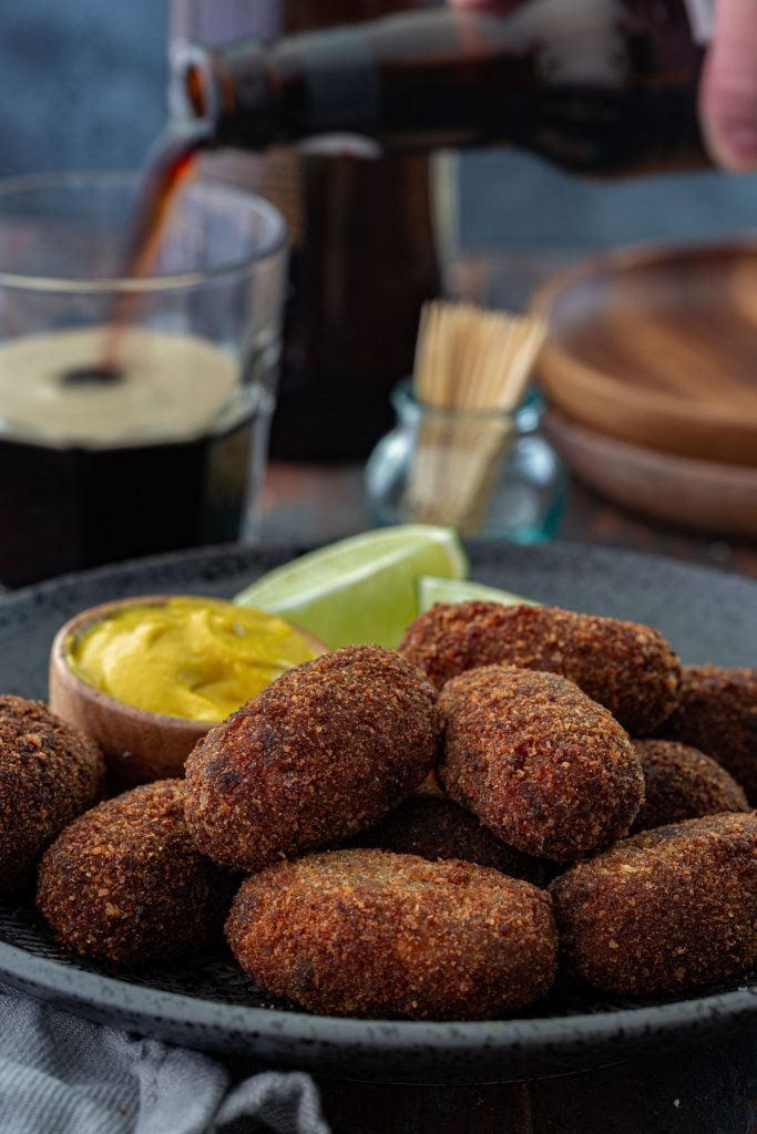 A platter of oxtail croquettes served with mustard and lime wedges.