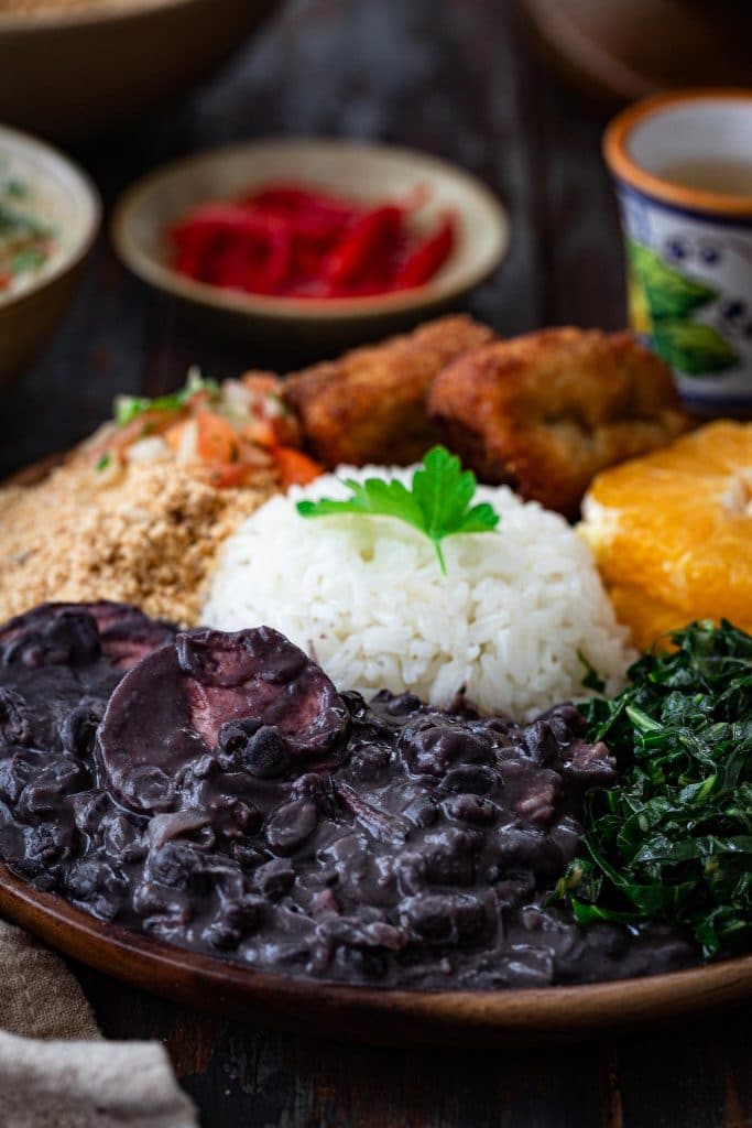 A plate of Brazilian black bean stew, rice, collard greens, oranges, farofa, fried bananas and salsa.