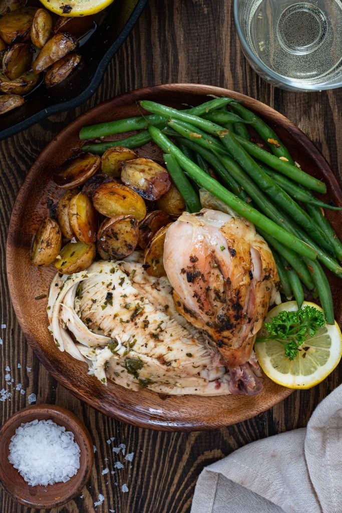 Roasted chicken dinner served with potatoes and green beans.