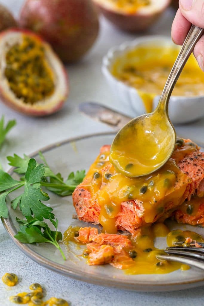 A photo of a hand spooning passion fruit on a pan fried salmon piece.