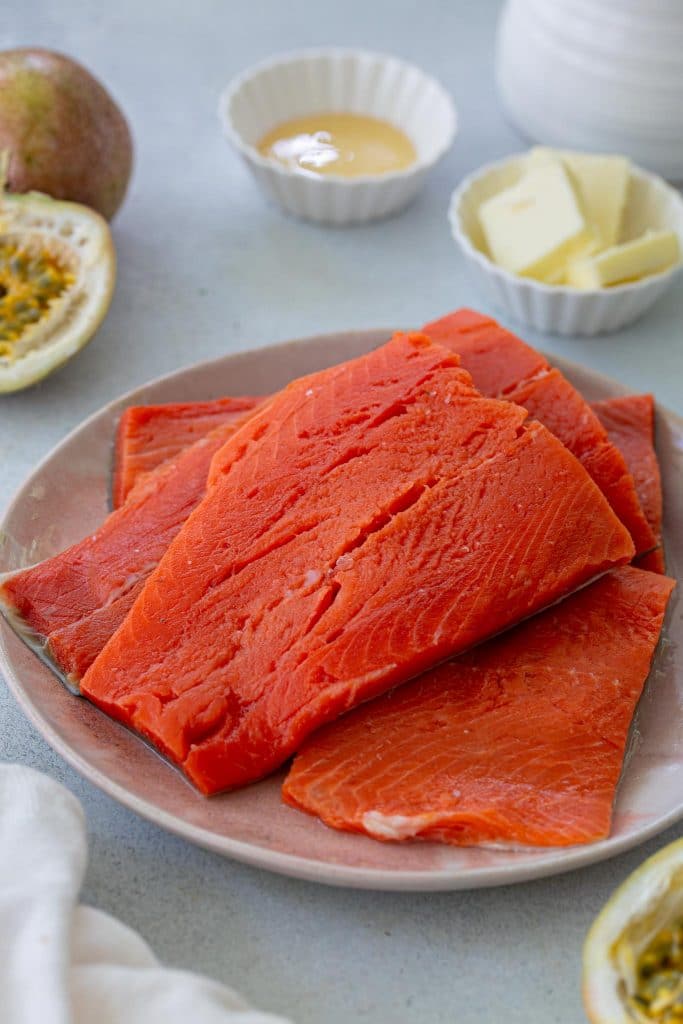 A photo of salmon. In the background: passion fruit, honey and butter.