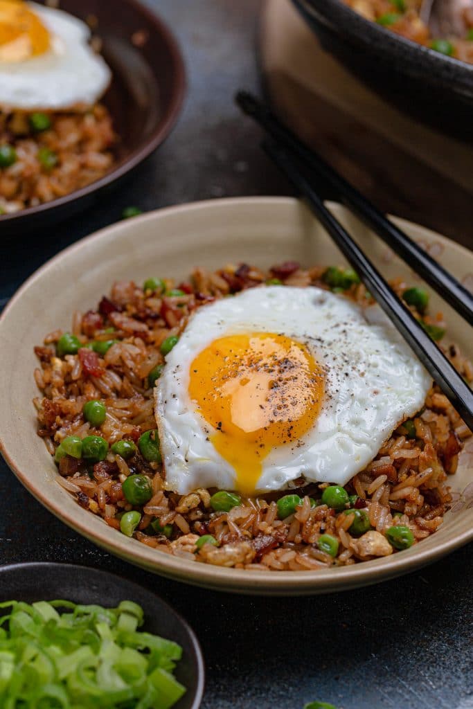 A bowl of bacon fried rice topped with a sunny-side up egg.