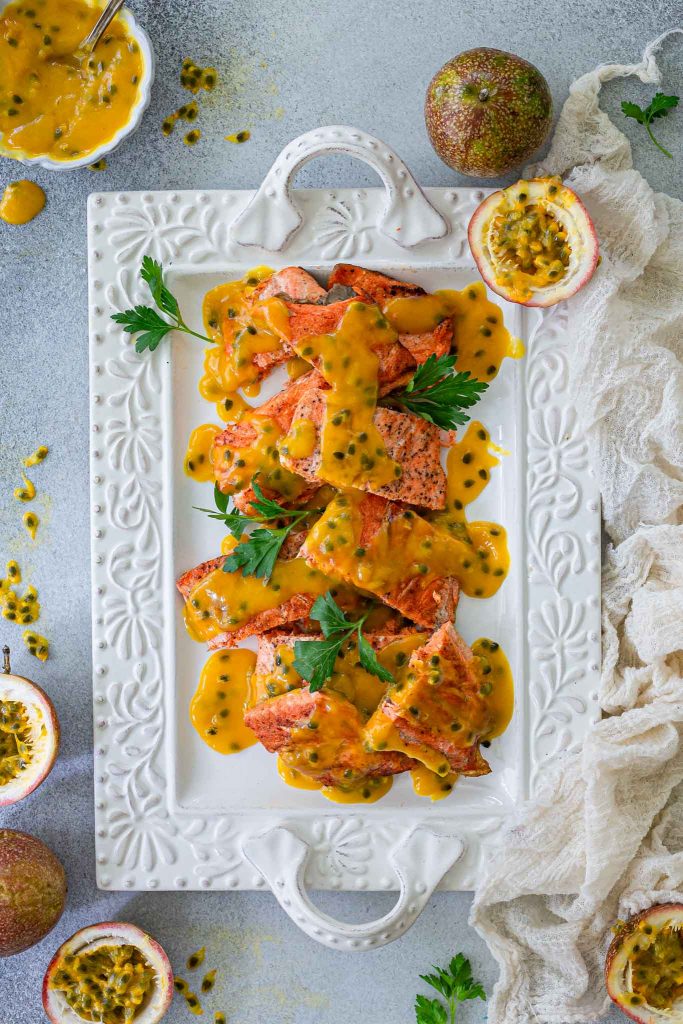 A platter with pan fried salmon with passion fruit sauce spooned on top.