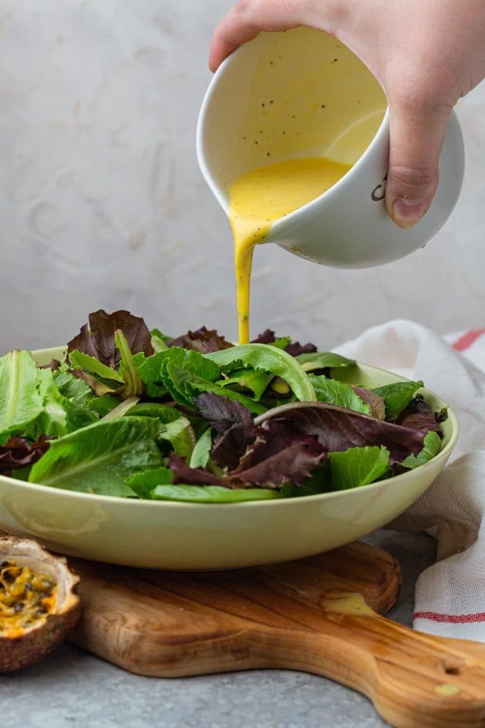 Pouring passion fruit dressing on a bowl of green salad.