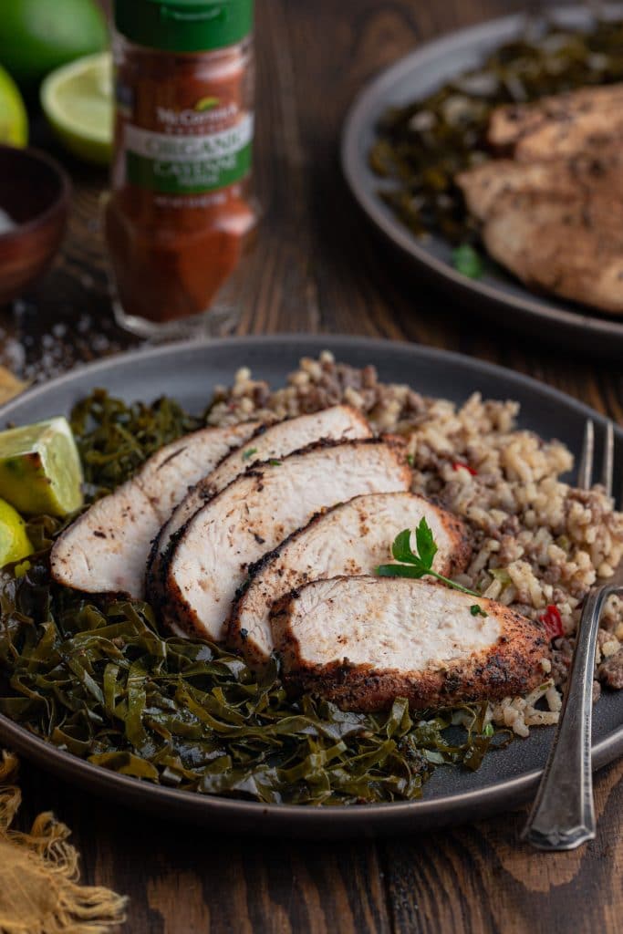 A shot of a serving of the dish: sliced chicken breasts, collard greens and rice.