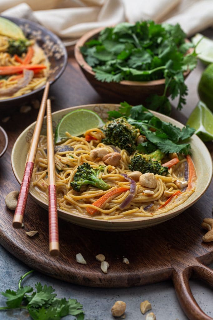 A bowl of cashew coconut curry noodles, garnished with a lime wedge and fresh cilantro.