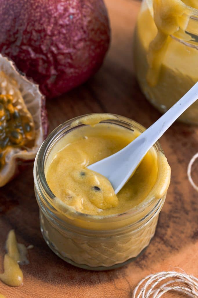 A closeup shot of a jar of passion fruit curd, with a spoon inside.