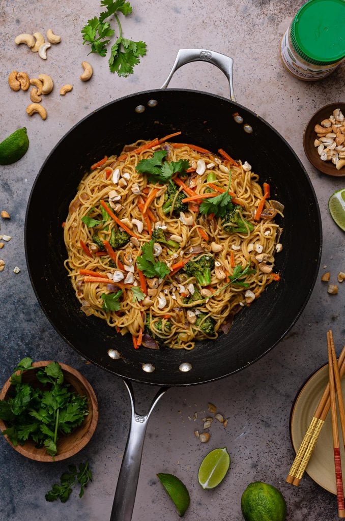 Curry noodles in the wok pan. Little bowls with garnishes can be seem on the table.