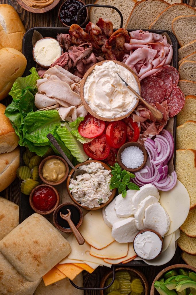 A build-your-own sandwich platter, with charcuterie, toppings, cheese and bread.