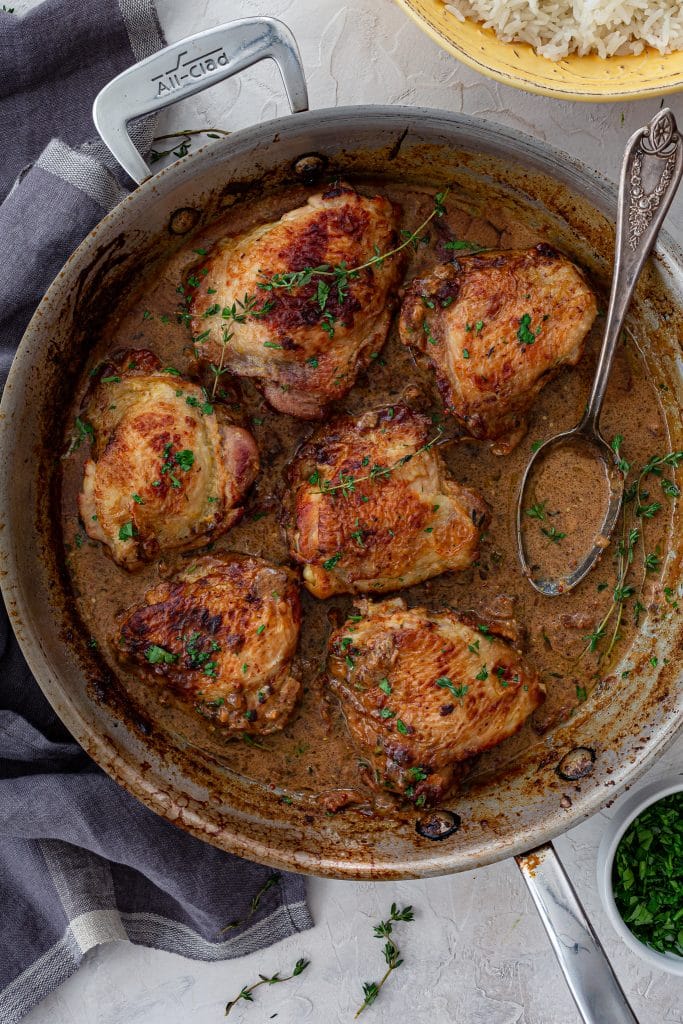 Poulet à la Moutarde in a skillet with a spoon with the sauce.