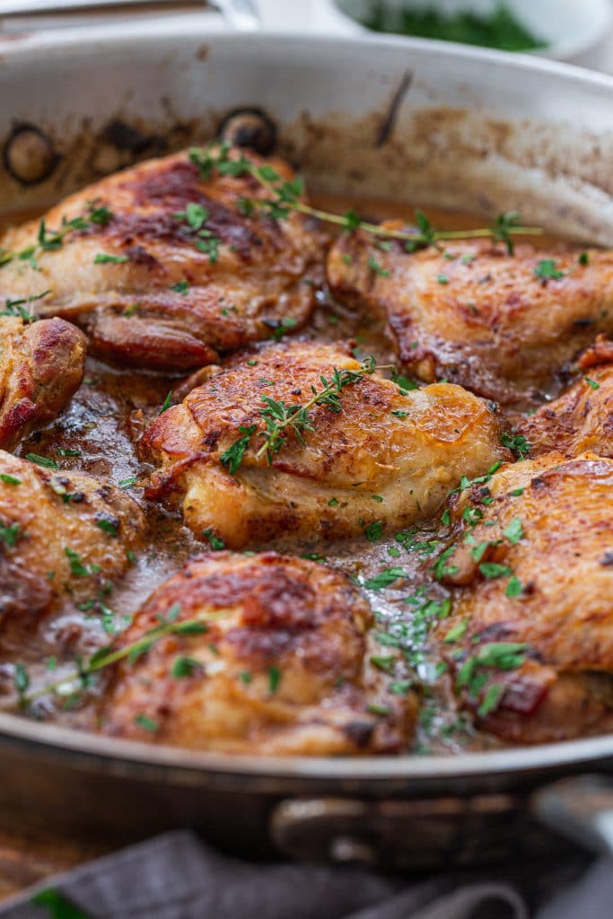 A skillet with French Mustard Chicken, garnished with thyme sprigs.