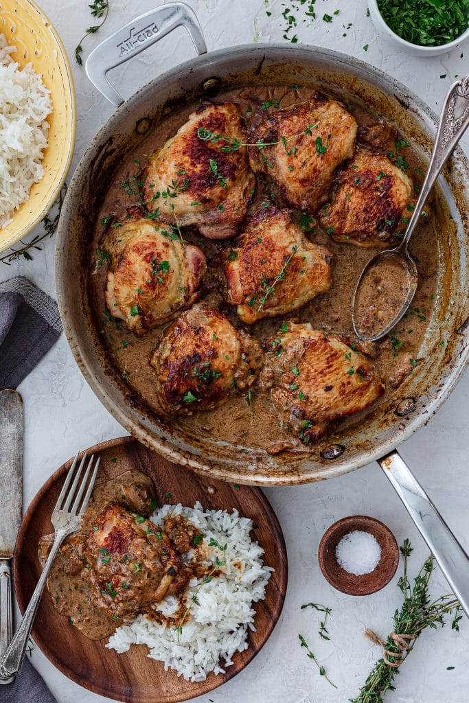 A serving scene: French mustard chicken in a skillet and served with rice in a small plate.