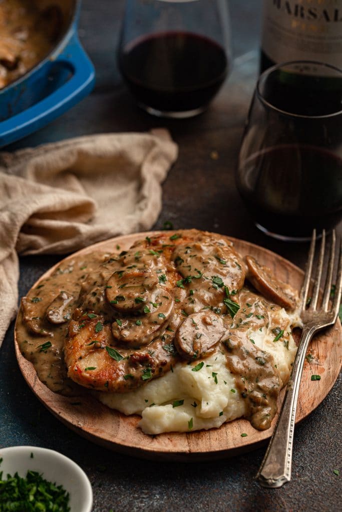 An individual portion of chicken marsala on a plate, over mashed potatoes.