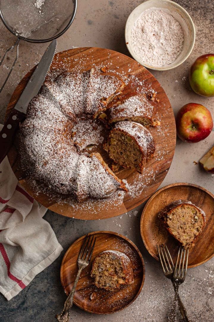 A serving scene. The apple bundt cake is sliced. Two slices in individual plates are shown.