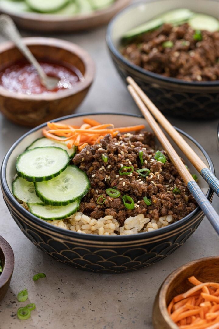 A Korean beef bowl topped with cucumber and carrots. Gochujang sauce on the sidel