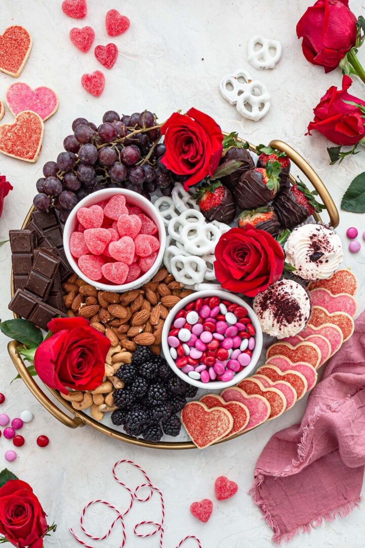 An overhead photo of a Valentine's Day Dessert Board, filled with cookies, chocolate, fruit, nuts, pretzels and roses.