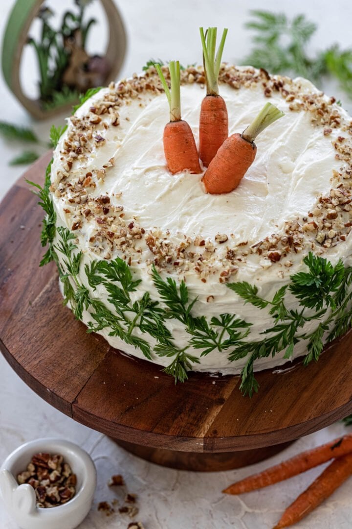 A beautiful classic carrot cake, decorated with chopped pecans, fresh carrots and carrot greens.