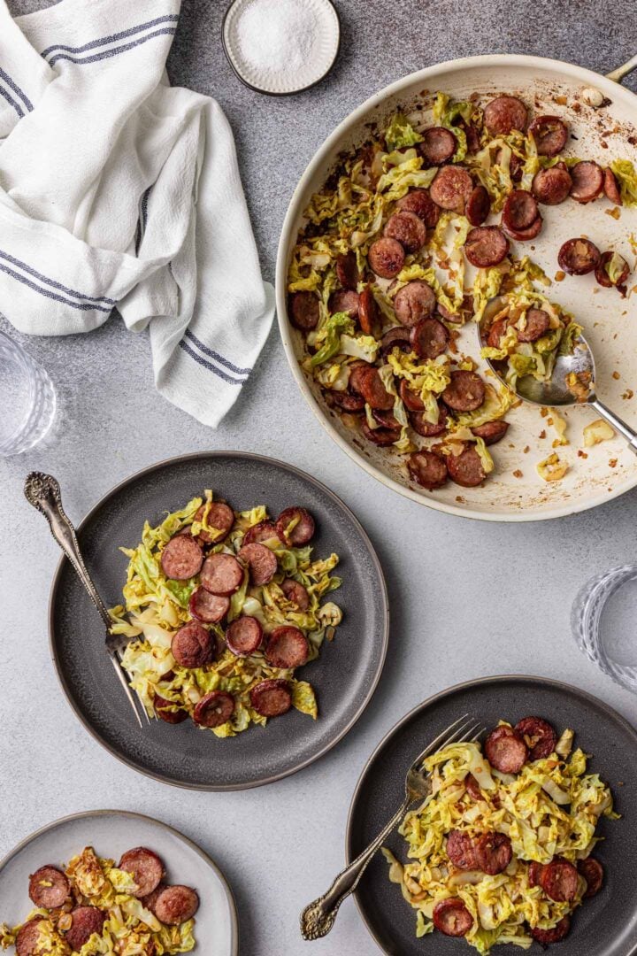 A serving scene. Sausage and Cabbage Skillet plus three individual plates with the sausage and cabbage.