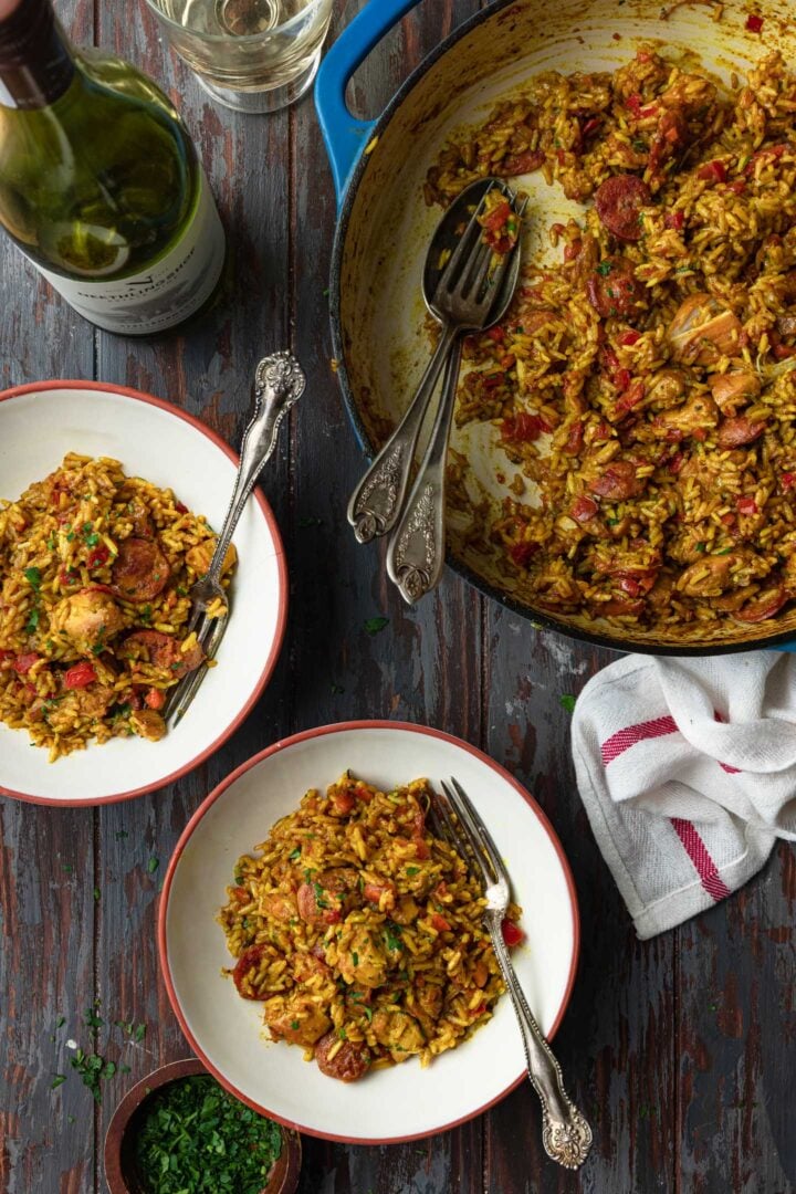 A serving scene: a pot of galinhada, a bottle of wine and two individual portions.