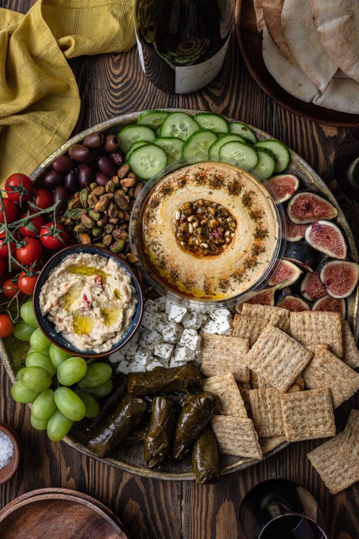 A beautiful mezze platter loaded with veggies, fruits, crackers, stuffed graped leaves, dips and nuts.