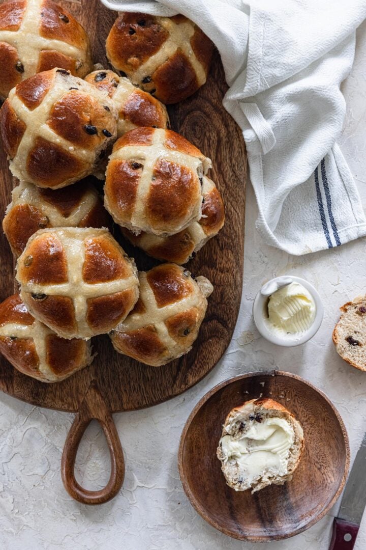 Hot cross buns on a wood board and a buttered bun on the side.