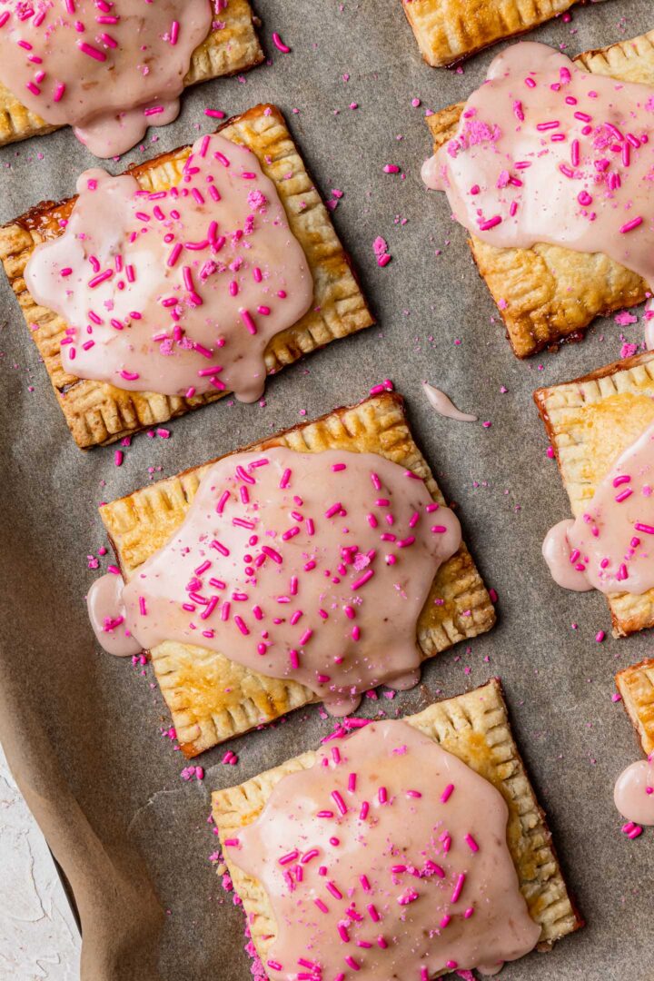 Toaster pastries iced with strawberry frosting, on a baking sheet.