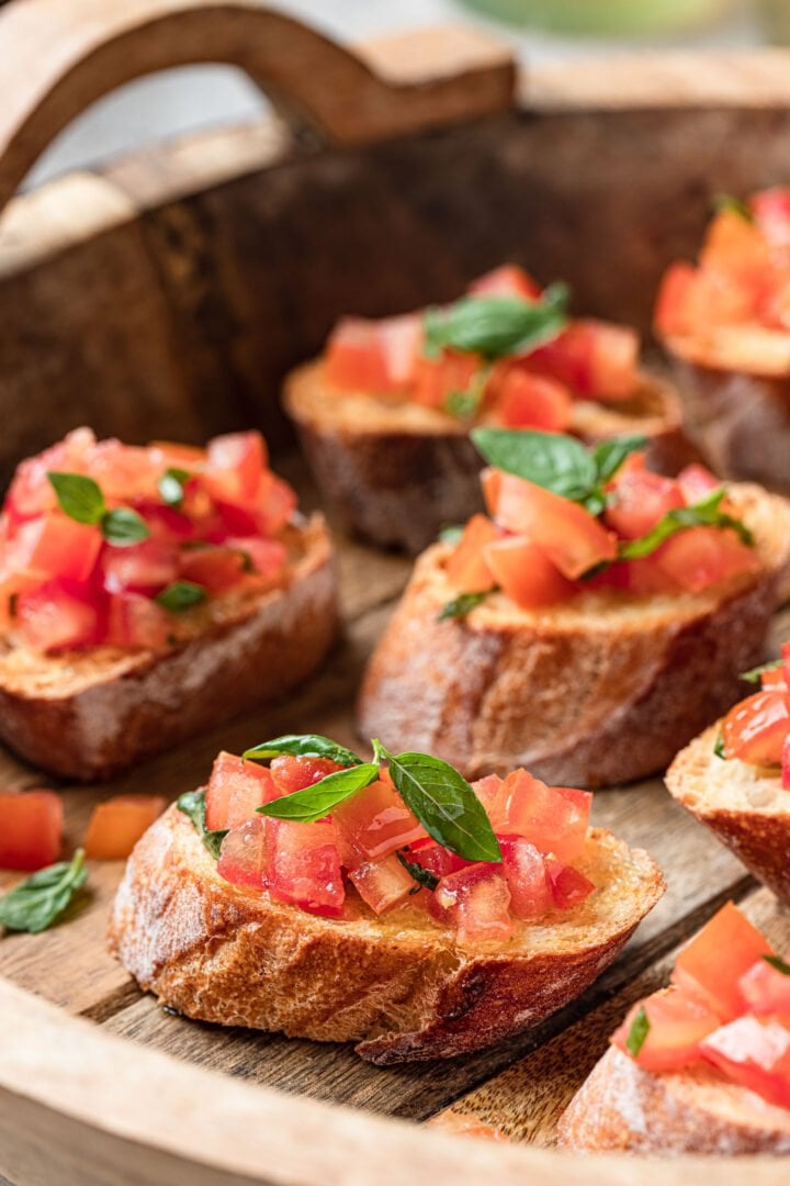 Close up of a wooden tray of tomato bruschetta garnished with basil.