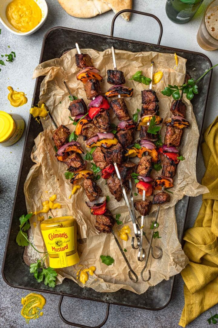 A tray of marinated steak kabobs and a bottle of mustard.