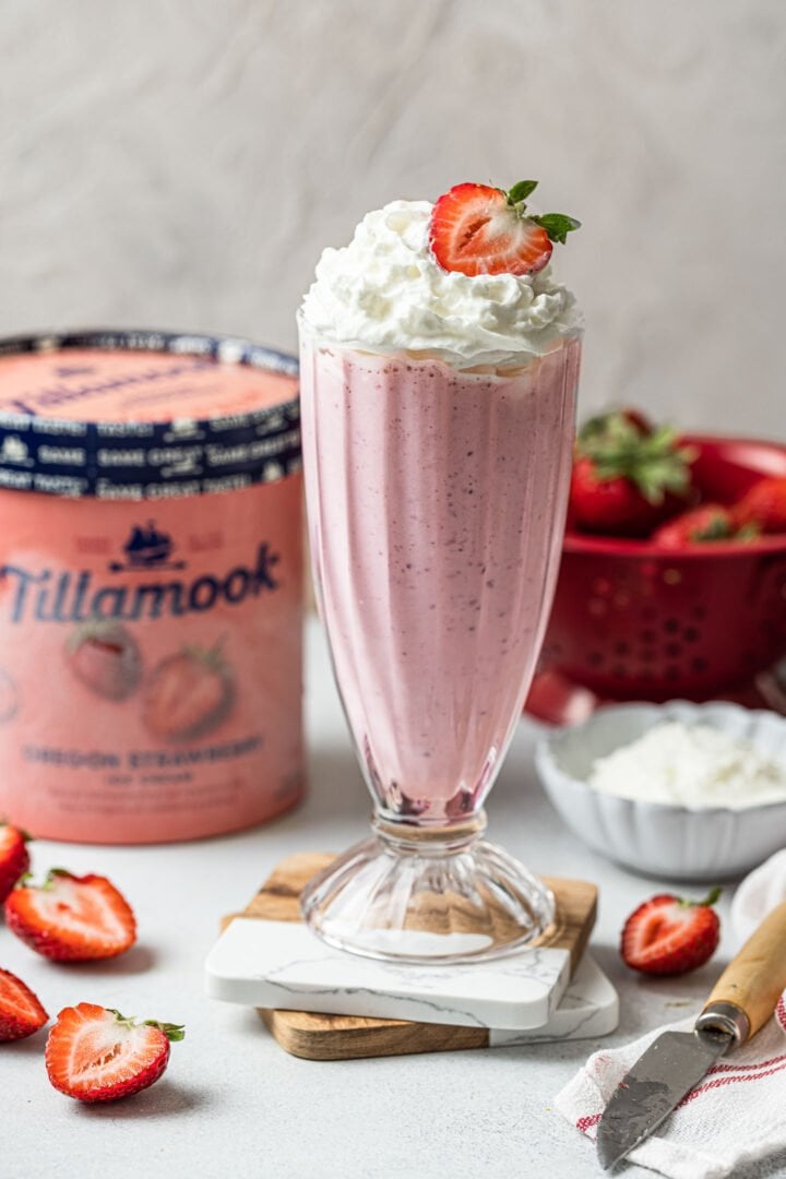 A glass of strawberry milkshake, topped with whipped cream and a strawberry.