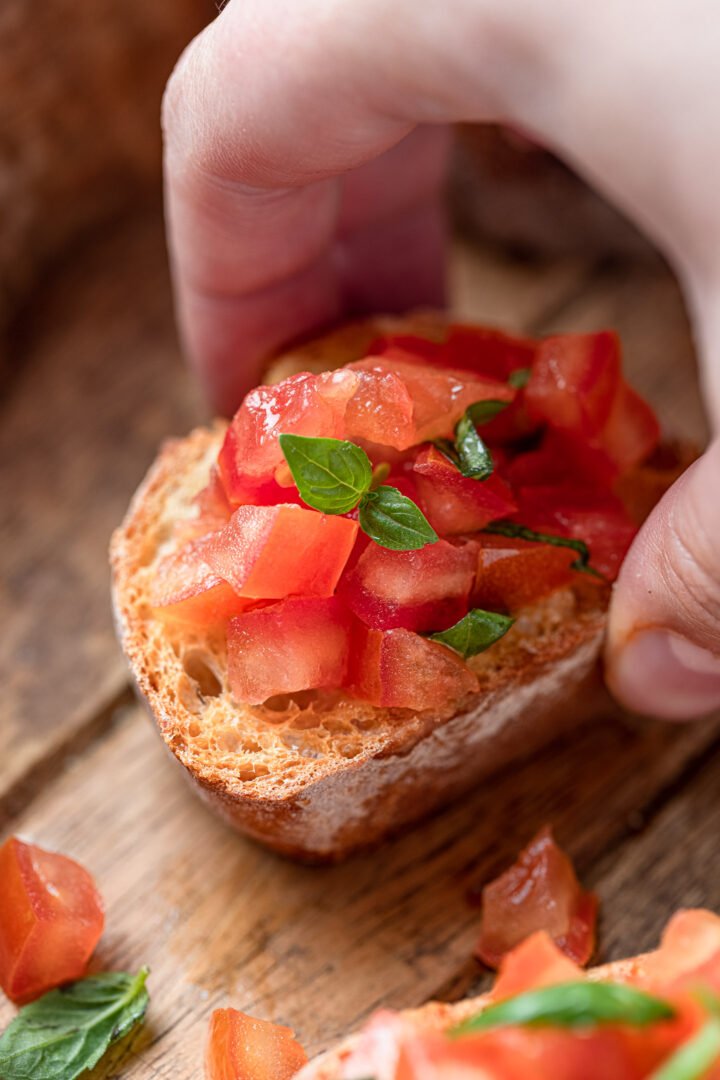 A hand picking up a tomato bruschetta.