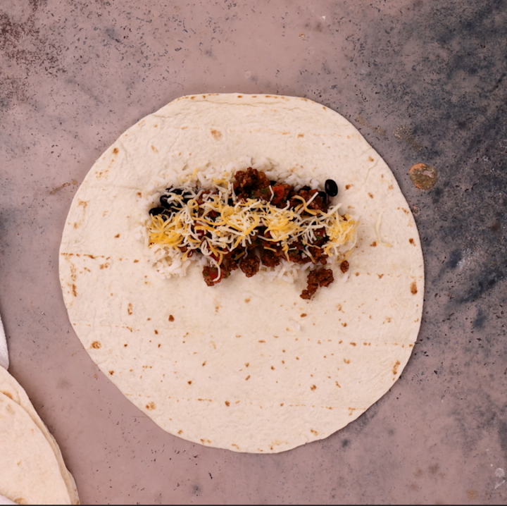 Assembling the beef burrito. Fifth layer: cheese.