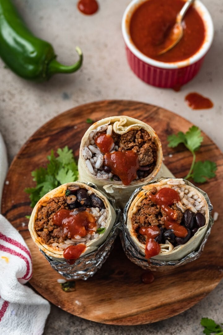 Three ground beef burritos drizzled with hot sauce.