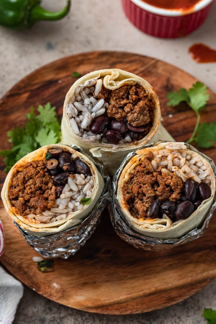 3 ground beef burritos halves on a plate. You can see the ground beef, rice and beans inside the burritos.