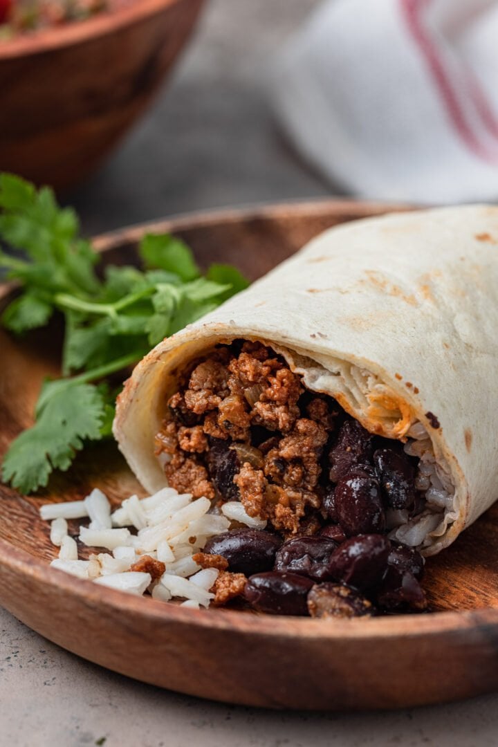 Rice, beans and ground beef spilling from a cut burrito.