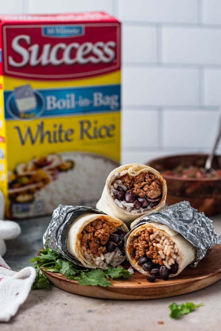 Ground beef burritos wrapped in foil with a Success rice box in the background.