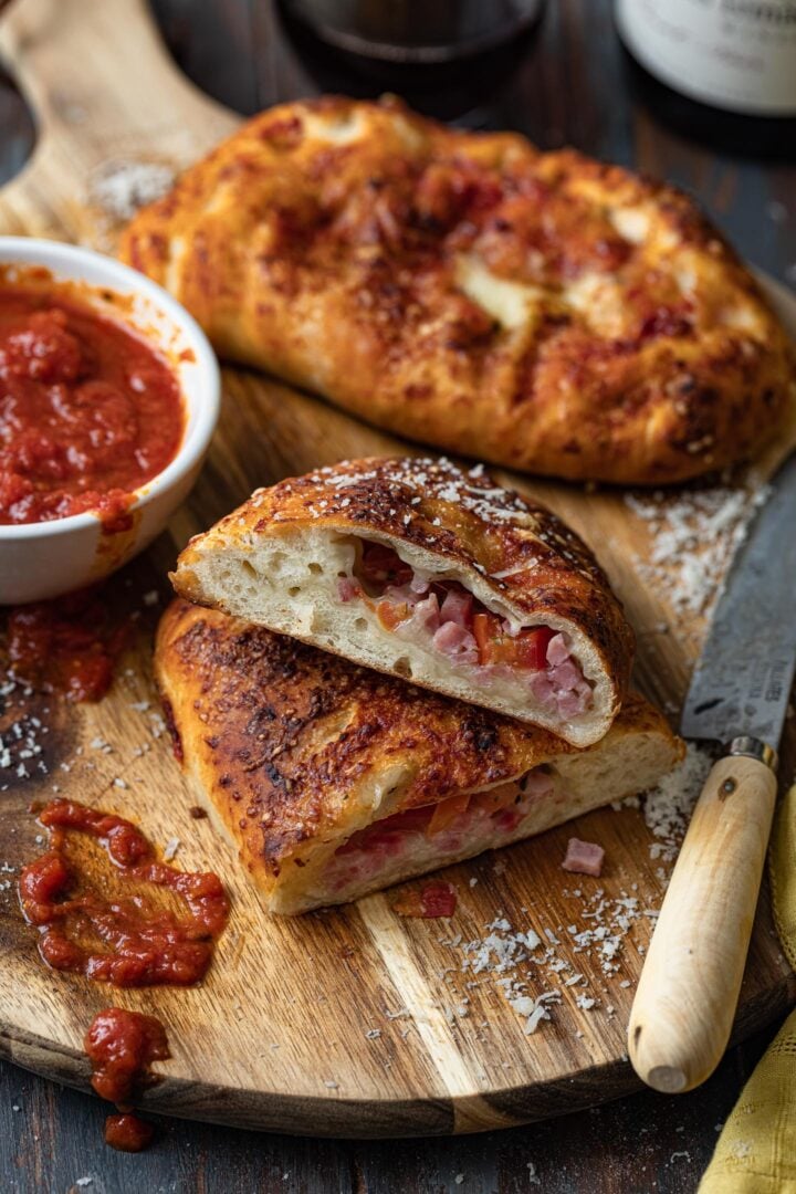 Ham and cheese calzone on a wood board, served with marinara sauce.