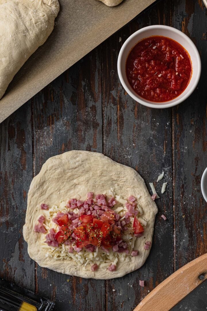 Layering the calzone: Tomato and oregano over the ham.