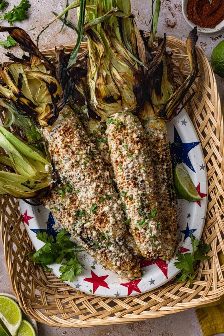 A tray full of elote, garnished with cilantro, chili powder and Cotija cheese.