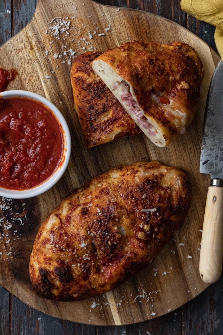 One whole calzone and one cut in half on a wood board