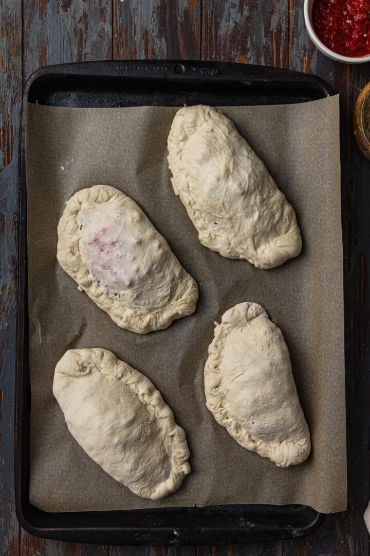 Raw calzoni on a baking sheet.