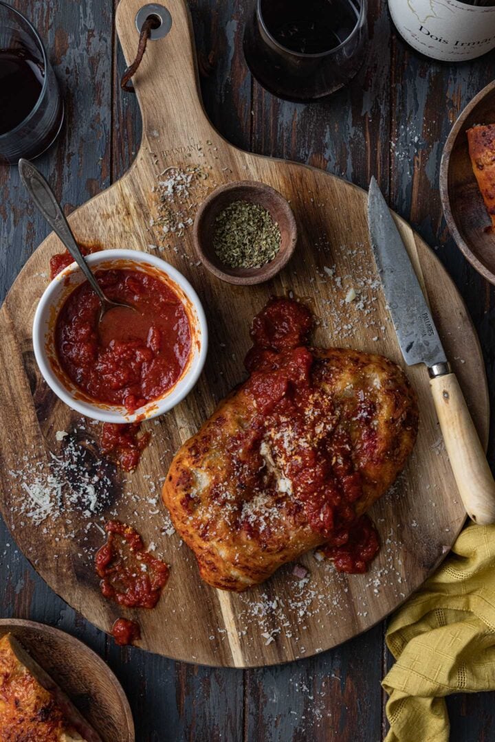 A calzone topped with pizza sauce on a board with a knife.