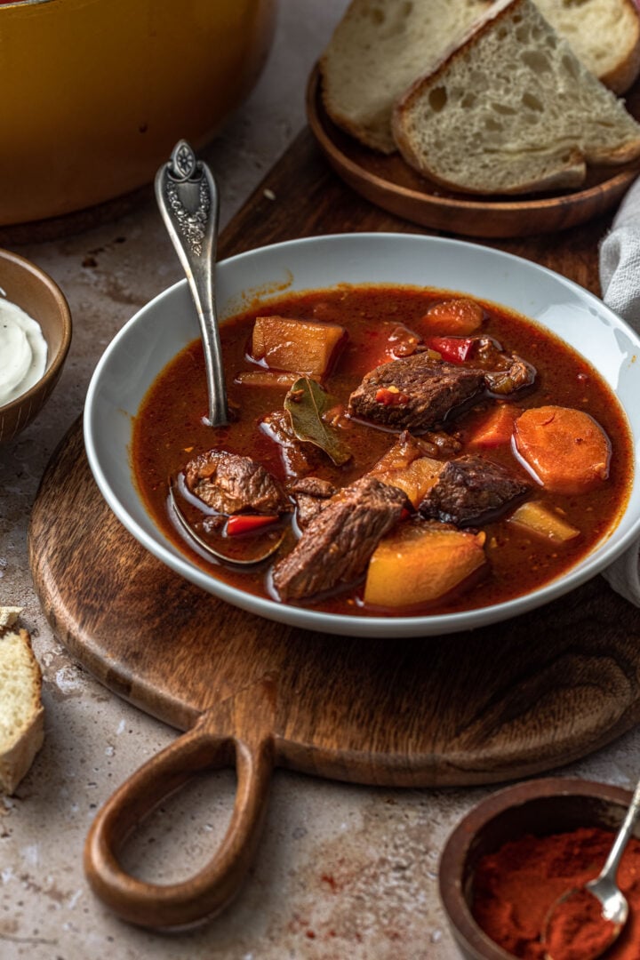 A bowl of Hungarian Goulash, served with a side of bread and sour cream.